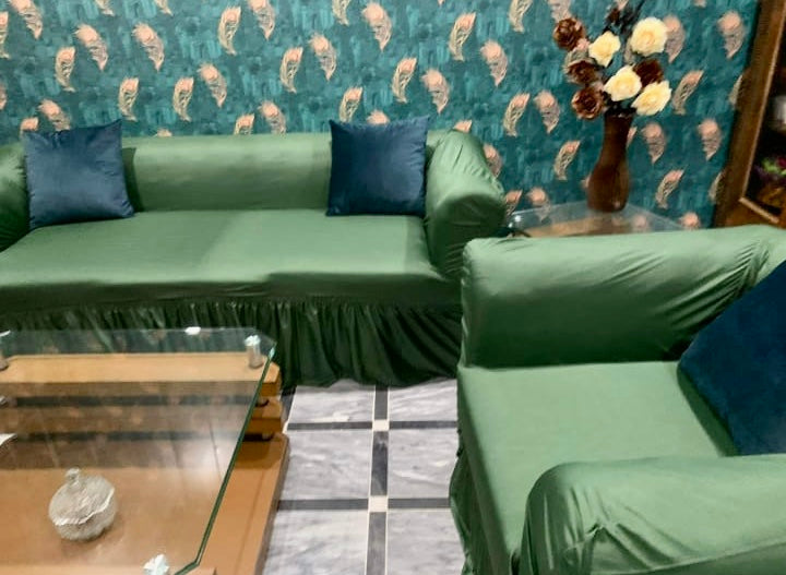 Green sofa with blue cushions against a patterned wall in a living room setting.