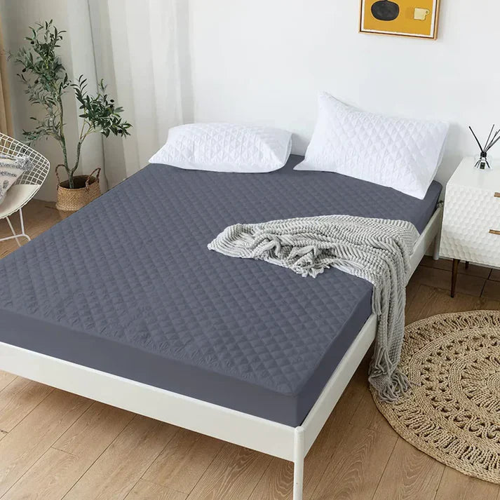 Gray quilted mattress cover on a bed in a bedroom setting with plants and decor.