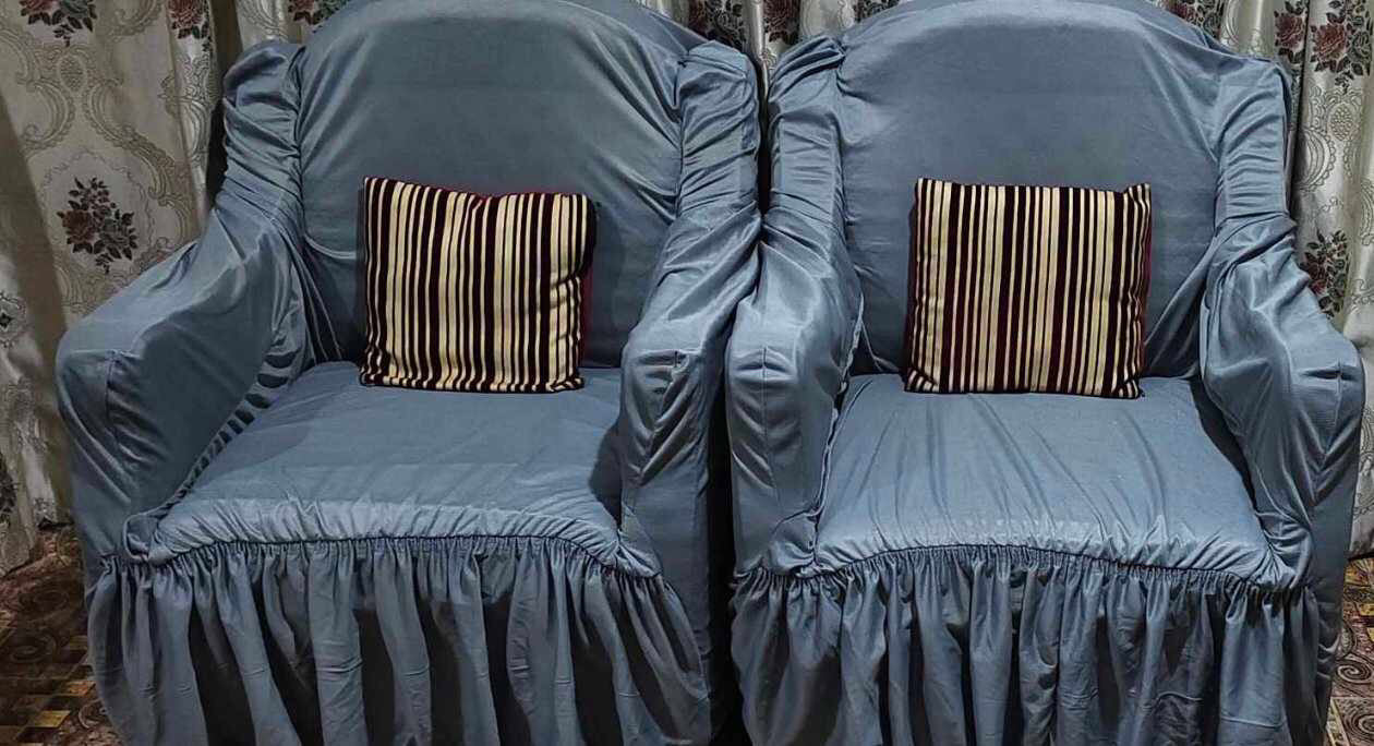 Two gray covered chairs with striped cushions on a patterned carpet.