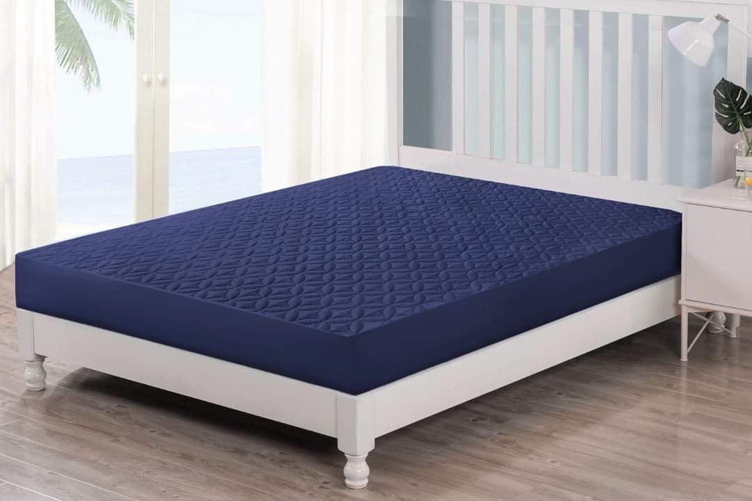 Navy blue mattress cover on a white bed in a room with large windows.