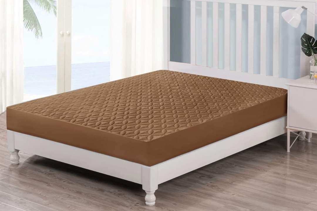 Brown mattress cover on a white bed in a room with large windows.