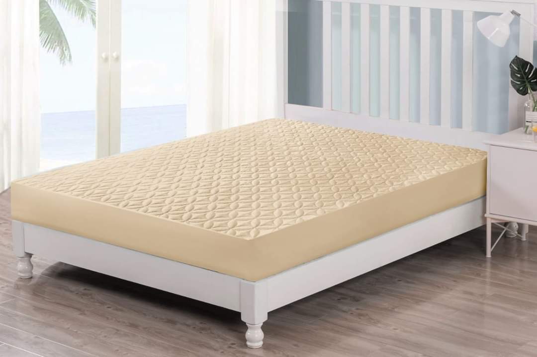 Beige mattress cover on a white bed in a room with large windows.