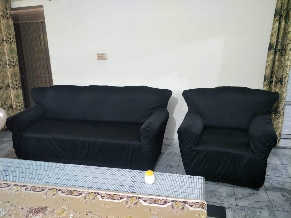Two black sofa covers on a couch and chair in a room with a tiled floor and patterned curtains.