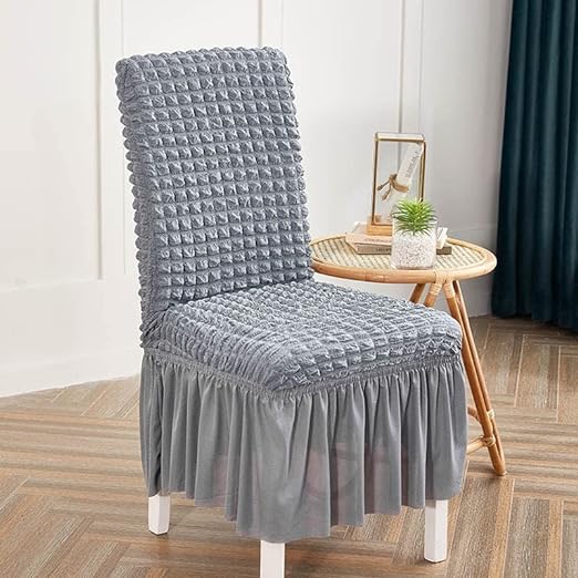 Chair with a gray textured cover in a room with a small table and decor items.