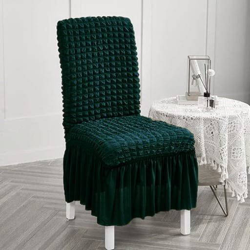 Green textured chair cover on a white chair in a room with a table and decorative items.