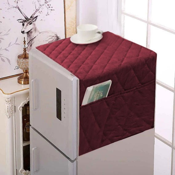 Maroon quilted cover on a white refrigerator with a cup and saucer on top.