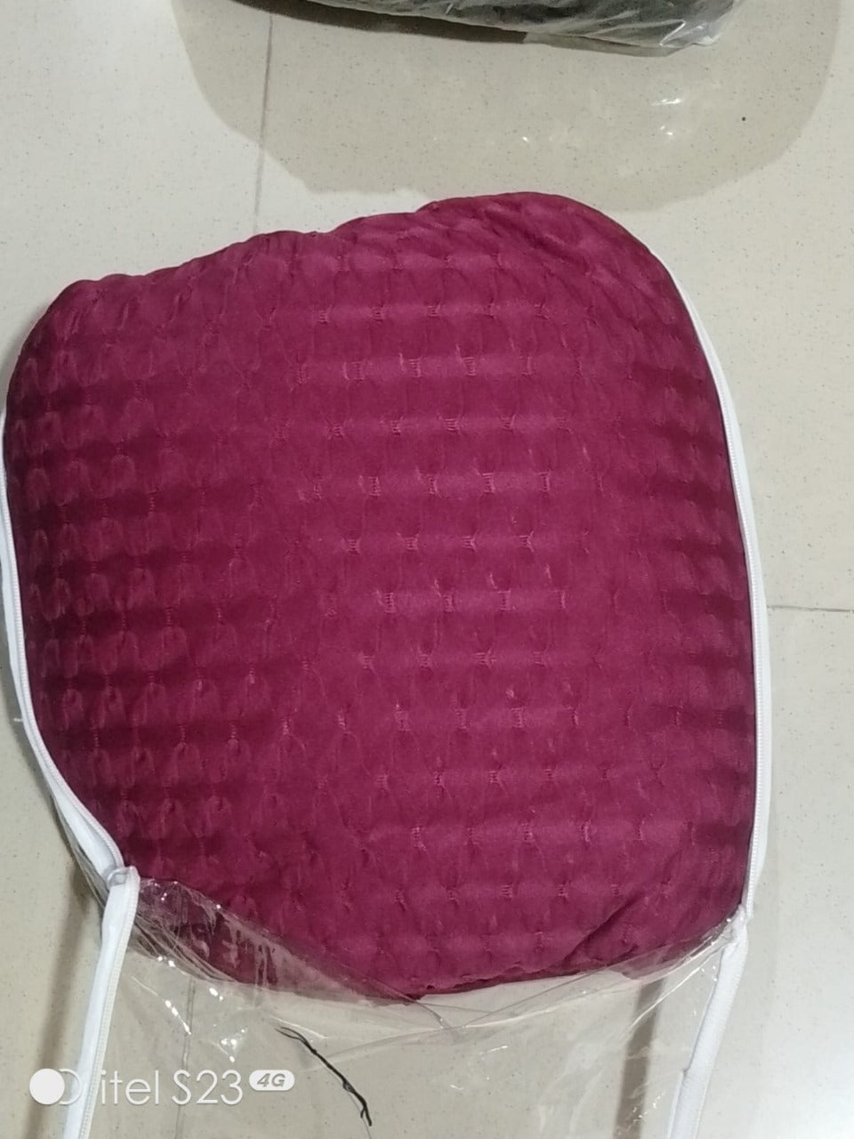 maroon cushion on a white surface with a clear plastic bag underneath